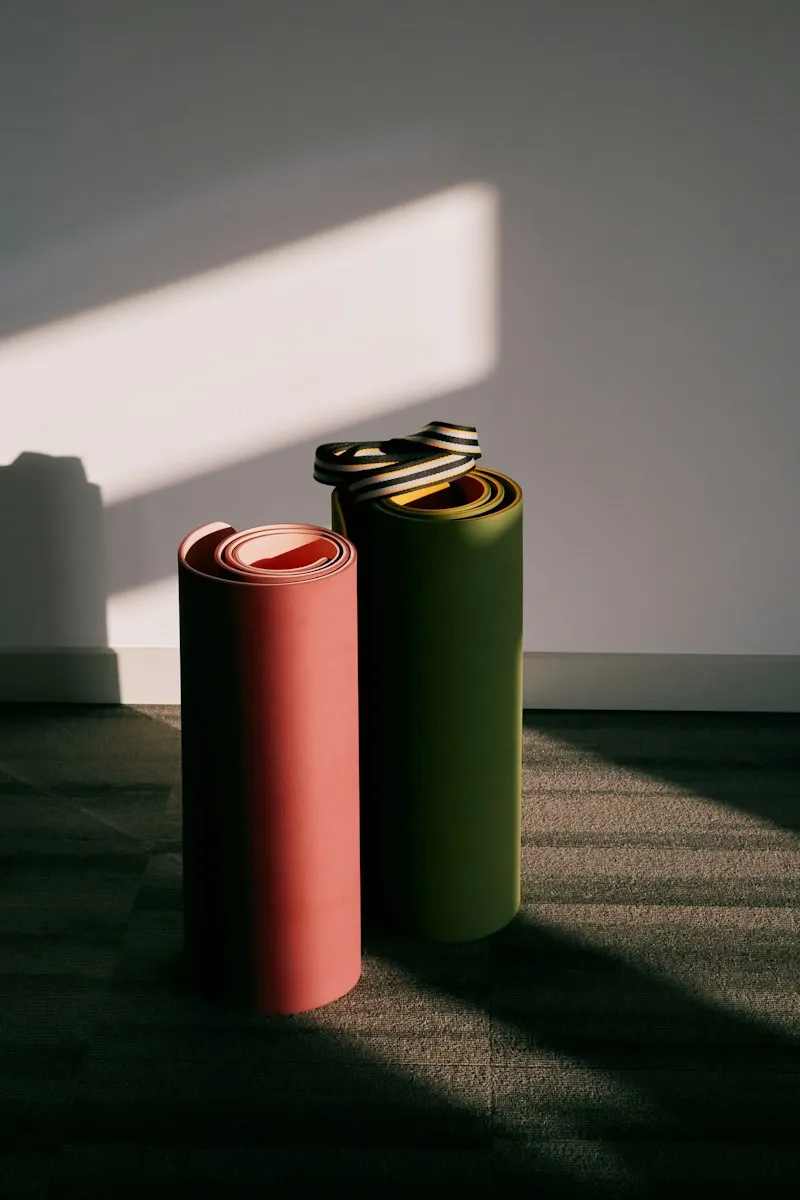 Two rolled yoga mats, one coral and one olive, standing in a patch of sunlight